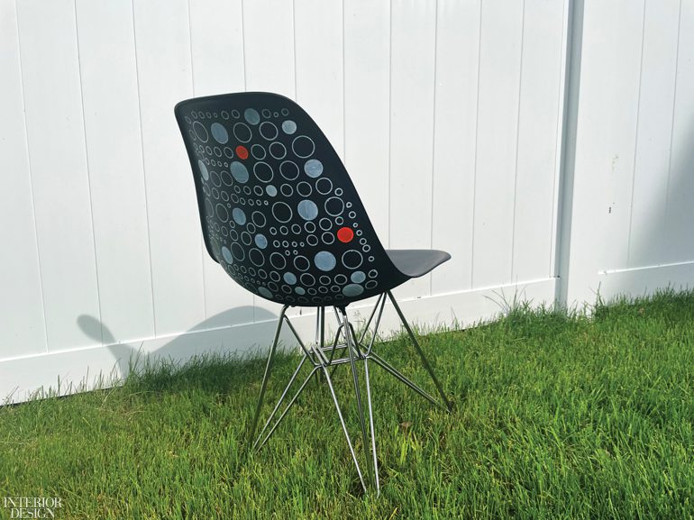 A black minimalist chair with colorful circles on the back on a bed of grass