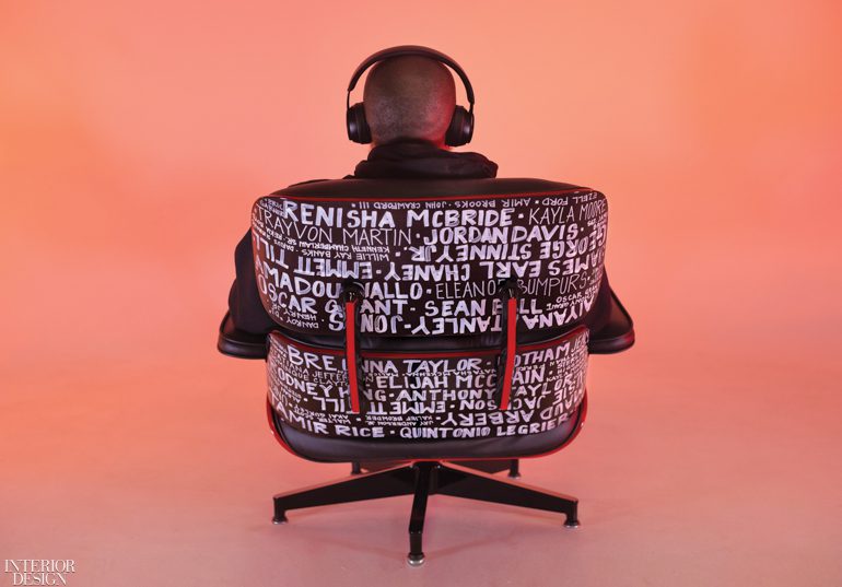 A Black man sits in a chair covered with the sames of victims of police brutality with his back turned and headphones on