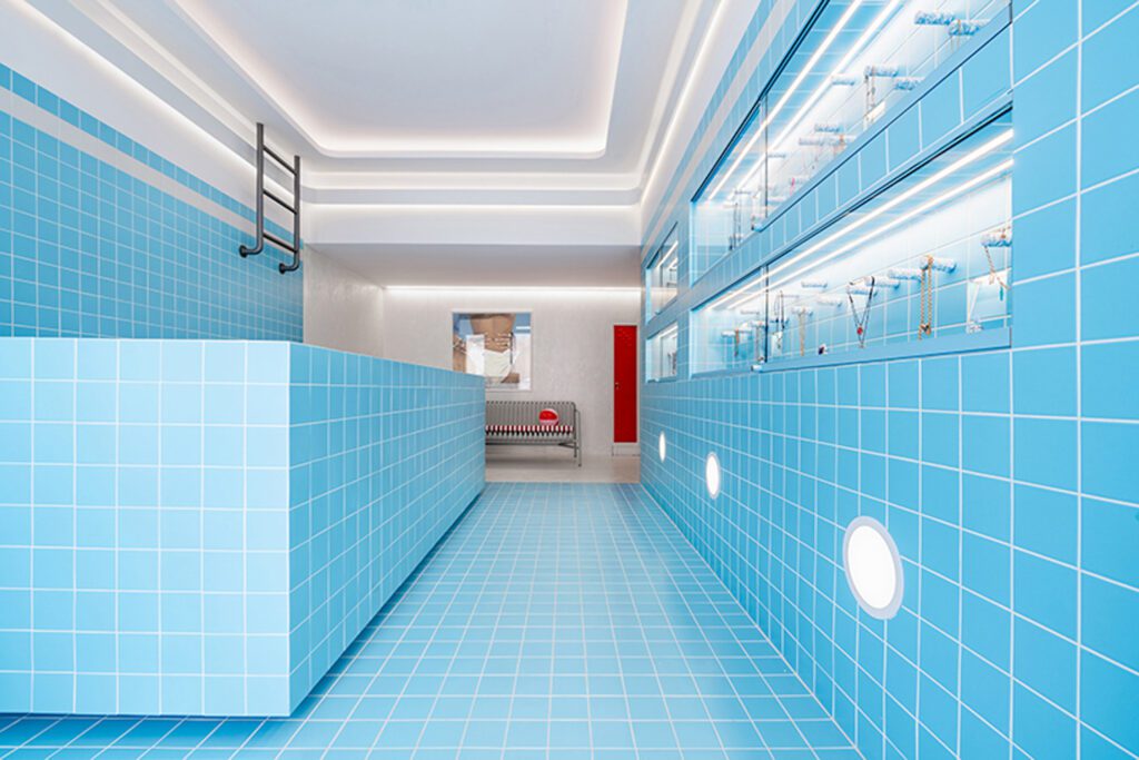 Shimmery turquoise ceramic tiles, rounded lights, a bench and red lockers further achieve a realistic swimming pool look. 