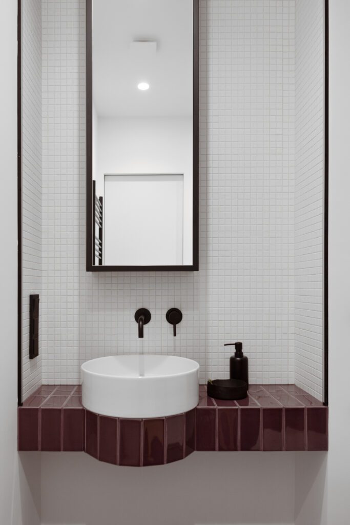 The bathroom console features a ledge for a round washbasin surrounded by tiles that match the floor.