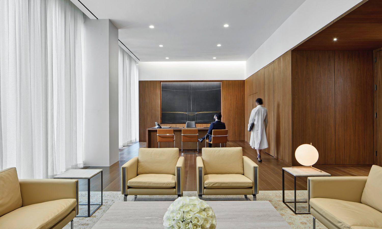 Wegner lounge chairs and sofas, Antonio Citterio coffee and side tables, and a custom rug form the seating area in an ambassador’s office, where a marble feature wall frames the custom desk and Mies van der Rohe side chairs.