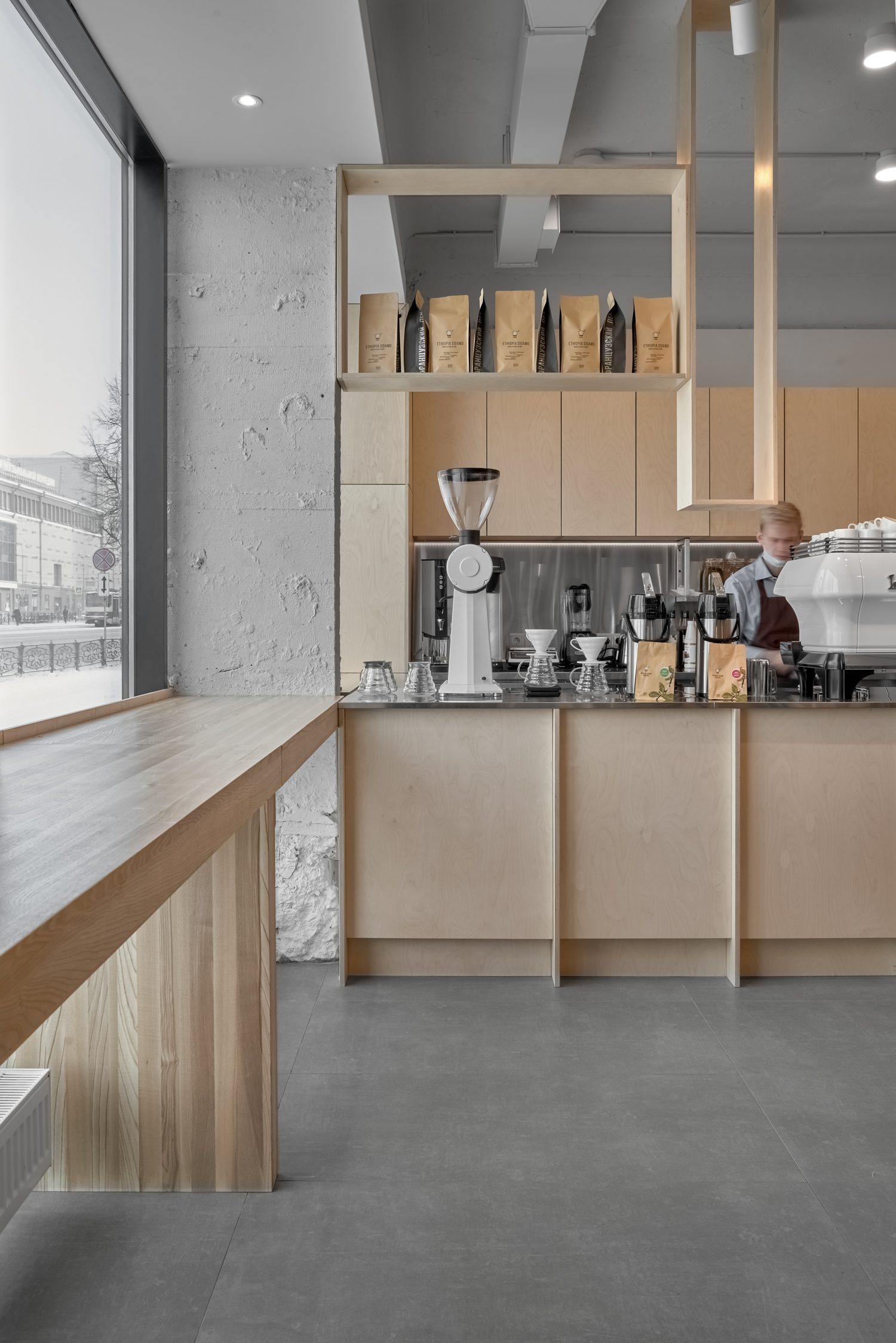 A cool palette of ash, plaster, and polished concrete keeps the focus on the steaming coffee behind the counter.