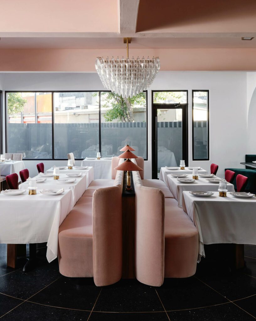 In the main dining room, the chandelier is by RH, pink chairs are by Crate & Barrel, red chairs are from 1stdibs, upholstery for the banquettes and chairs was completed by Under Cover Upholstery, and Litmus Industries fabricated all the banquettes and red chairs.