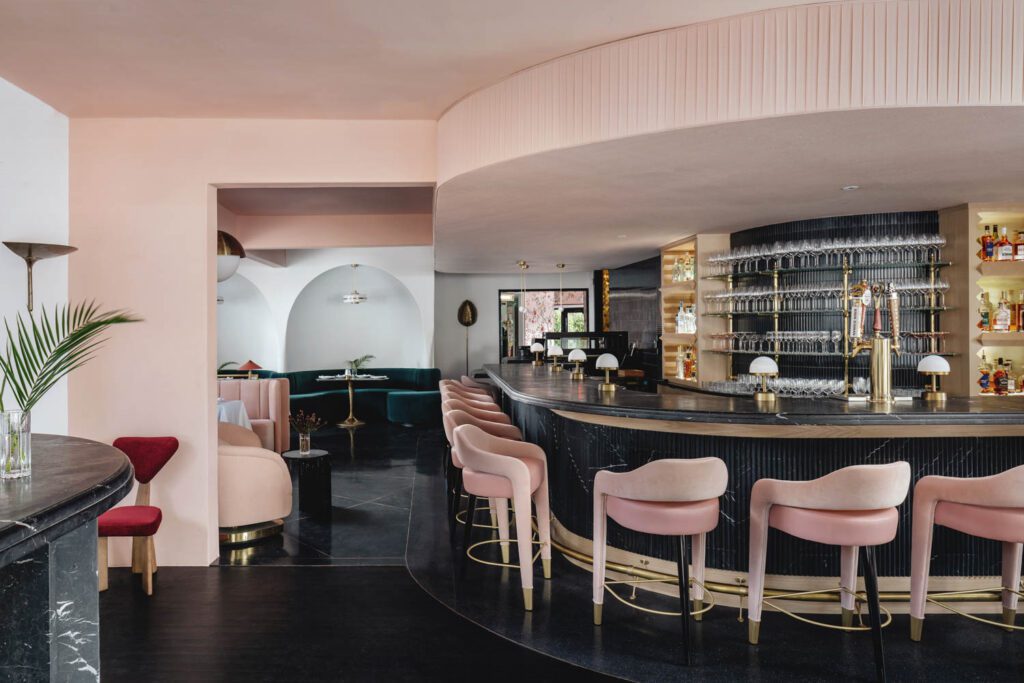 The bar is surrounded by fluted tile by Artistic Tile, custom cabinets by Madera Millwork, footrest by Kegworks, pendants by Future Perfect, with wall and ceiling paper by Ballard Designs.