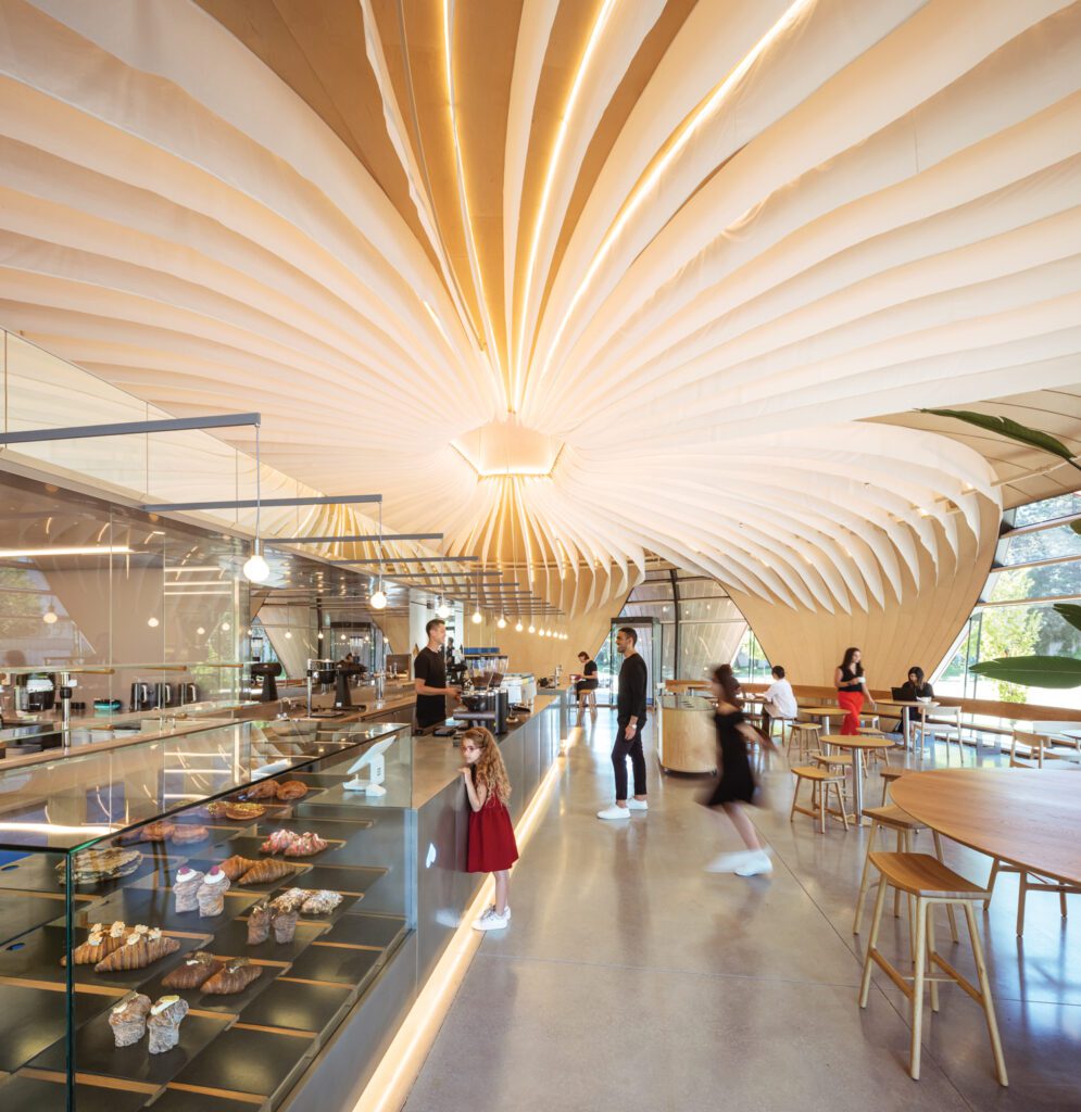 Flooring is polished concrete and baked goods are visible through the clear glass section of the partition.