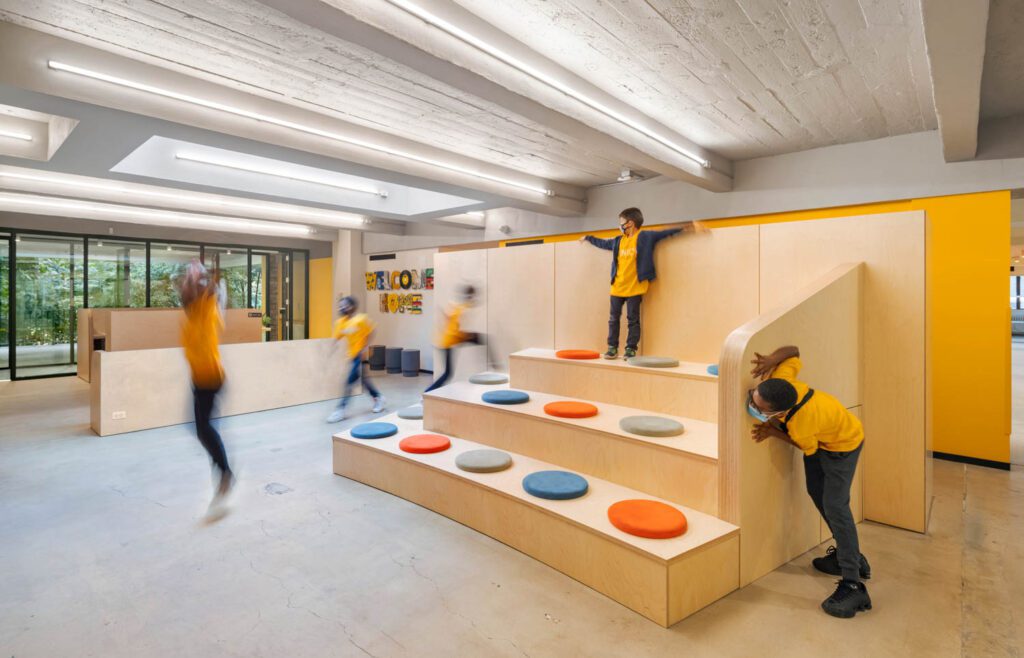 An expanded reception area full of natural light from new skylights opens to a multiuse space with stepped bleacher-style wood seating with pops of brightly colored art and finish accents.