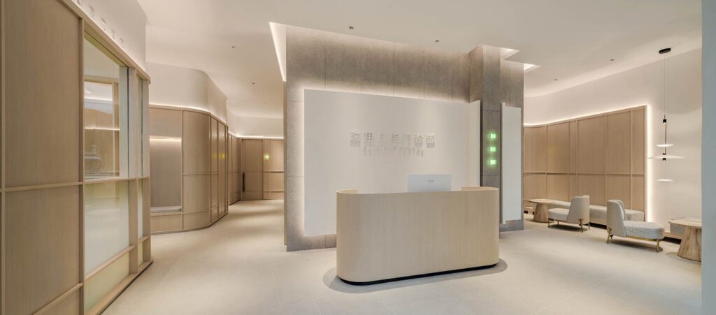 A reception desk of boxwood veneer floats before white relief-panel logo wall and a second wall clad in dark gray tile by Porcelain Tile.