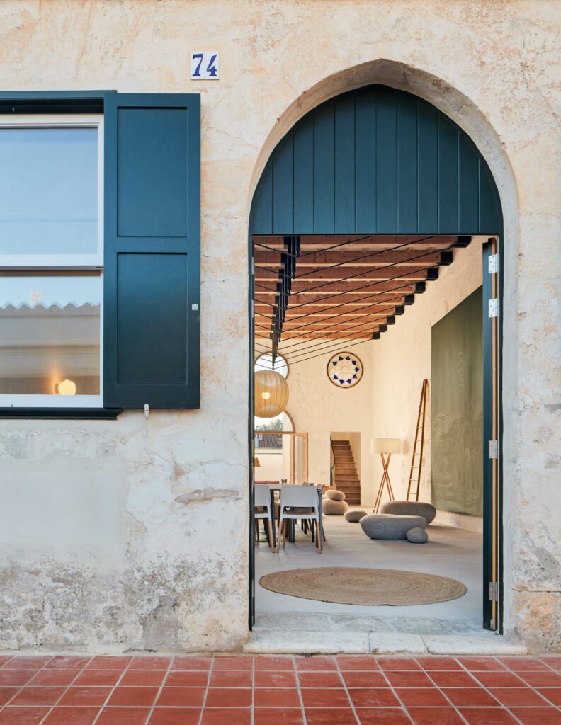 An arched front door next to a window with shutters open