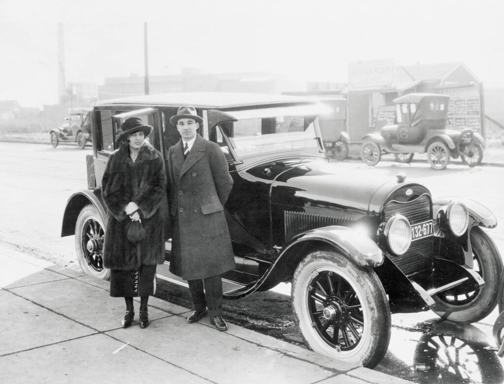 A black and white photo of a couple next to a vintage looking car