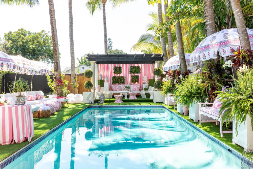 A pool surrounded by pink and white striped umbrellas, tables, and pool house