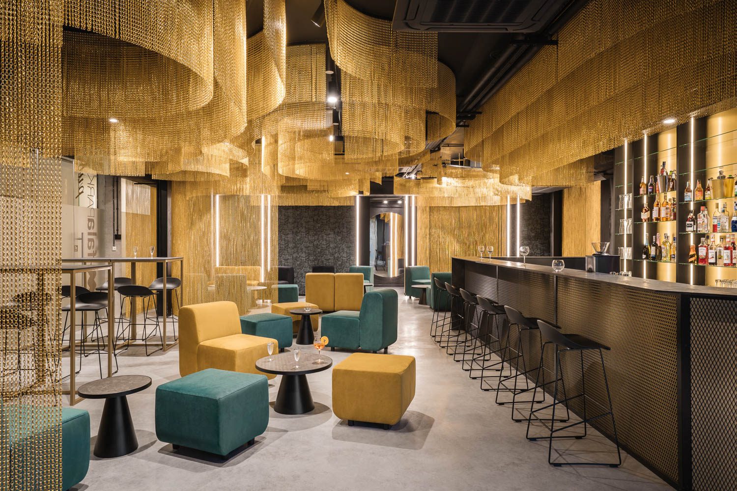 The bar at Fala Park by PL.architekci has aluminum chains hanging from the ceiling painted a shimmering gold.