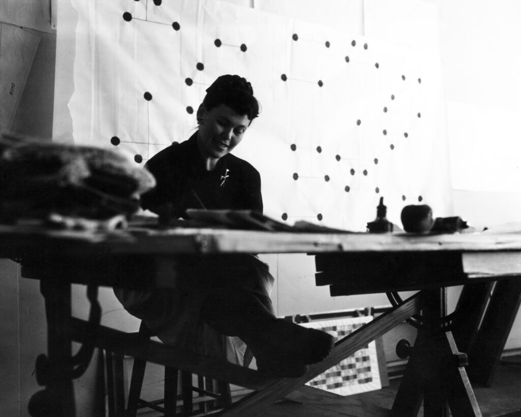 Black and white image of Ray at a desk in front of the dot pattern for the Reebok x Eames Office collaboration.