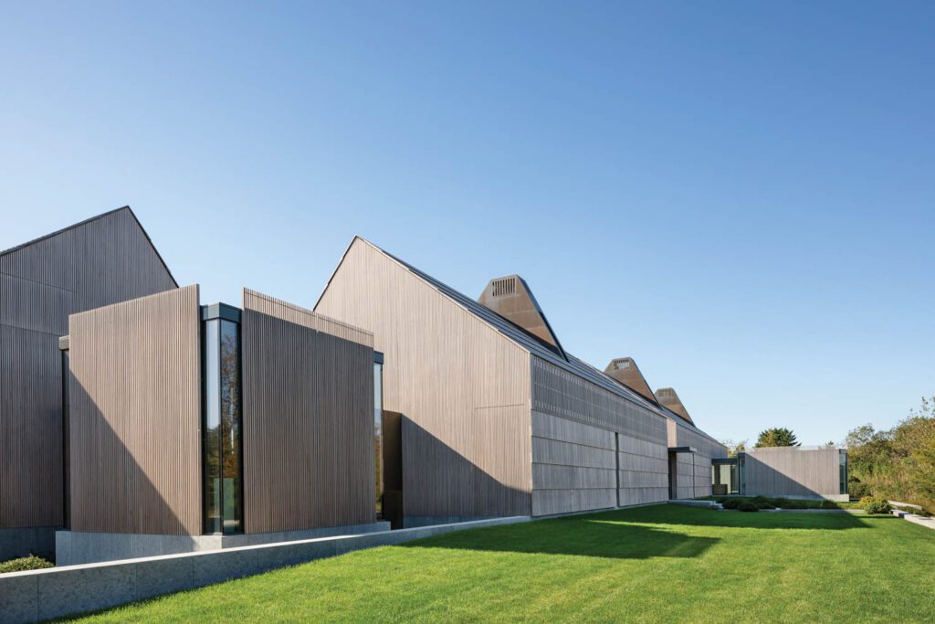 Connecting perpendicular sections of the three-building house, a glass cube screened with cedar slats also functions as sculpture gallery.