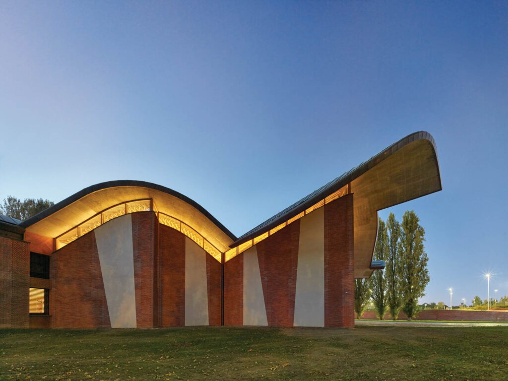 At night, light shining through the clerestory windows outlines the undulating roof.