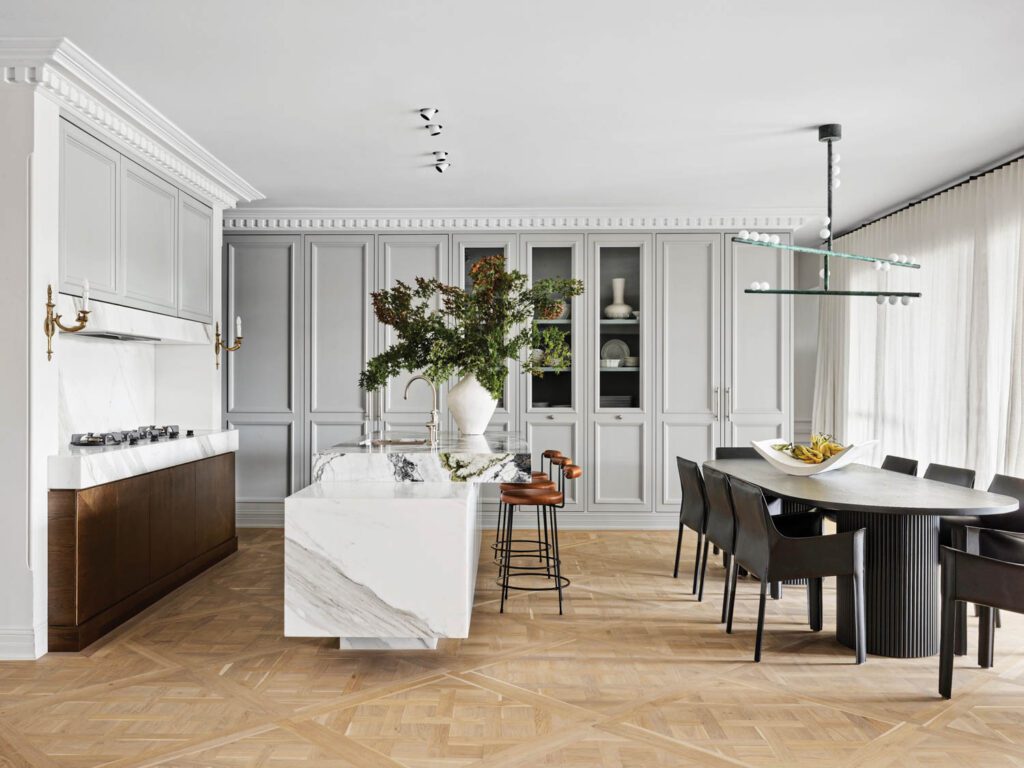 A papier-mâché vase by McMullen & Co. tops the kitchen island, which pairs Verde Chambray and Calacatta marble; the dining area’s Lindsey Adelman chandelier sports a copper patina finish.