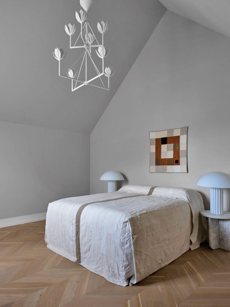 Acrylic lamps and a tiered chandelier by Julie Neill illuminate the guest bedroom.