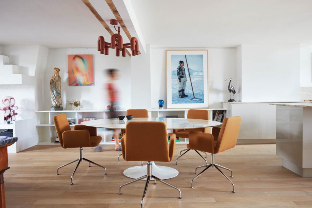 a dining room with orange chairs with a pink geometric chandelier overhead