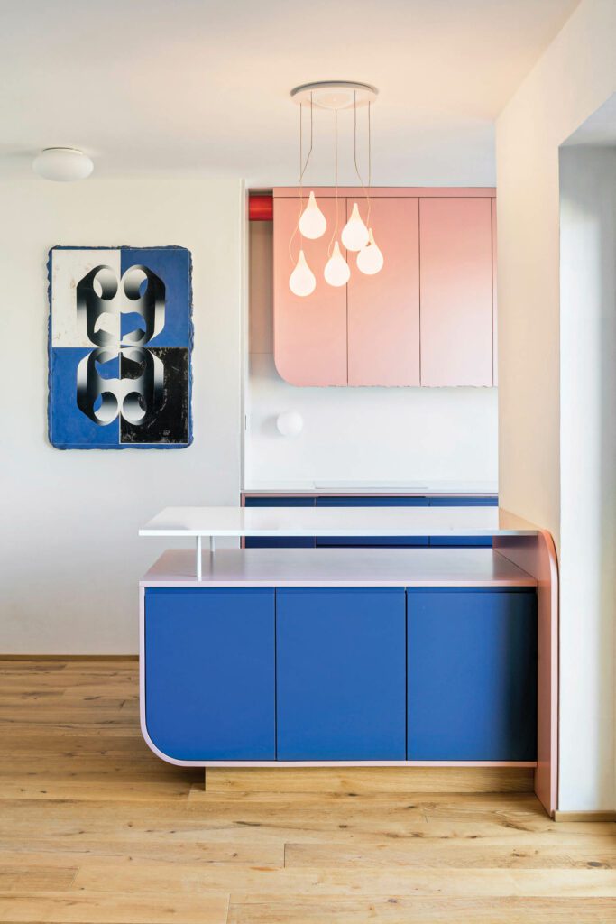 a blue kitchen island with a teardrop-esque chandelier overhead