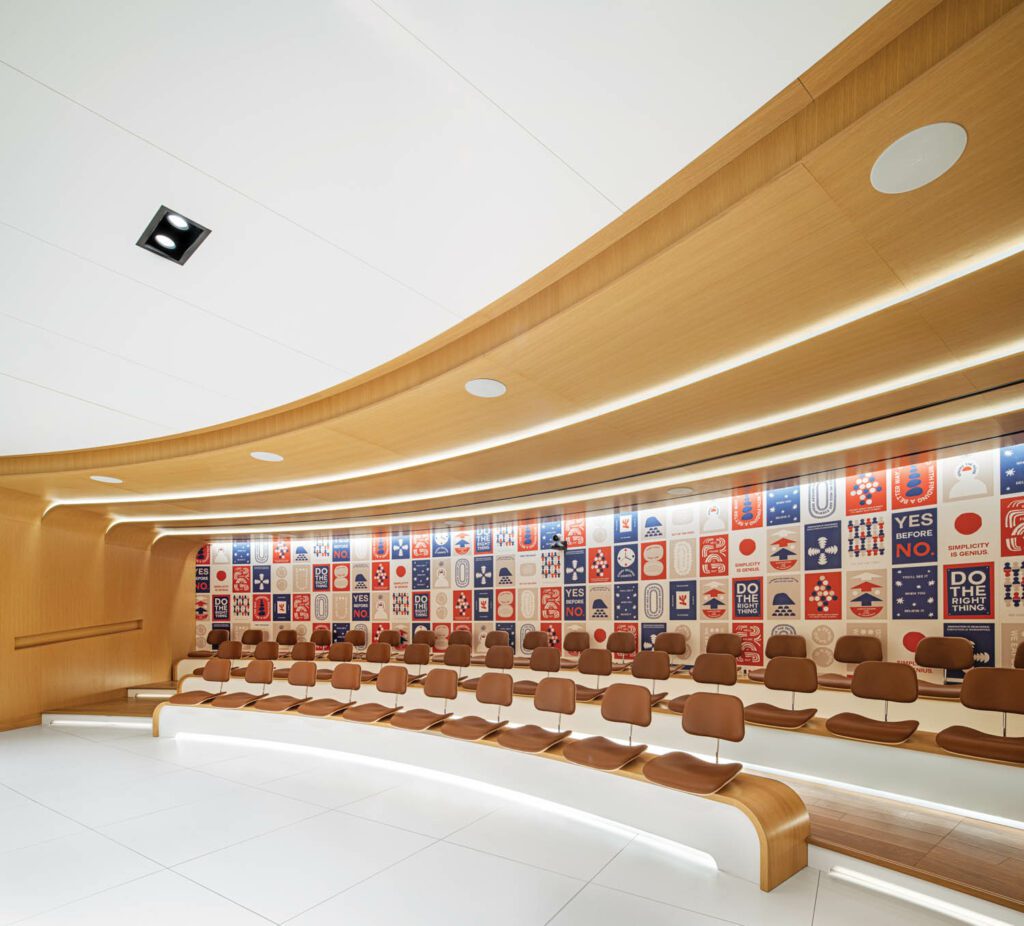 Leather-covered molded plywood chairs by Charles and Ray Eames have been mounted, without legs, on benches in the auditorium and backed by a Cody Hudson mural printed on acoustic panels.