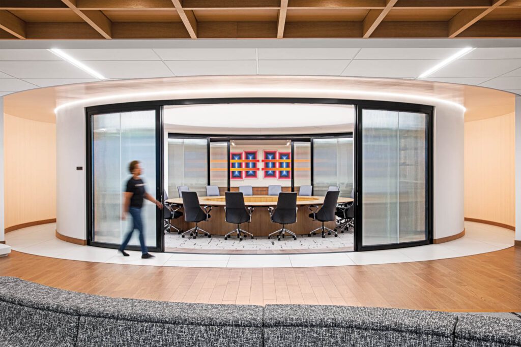 Textured glass doors open onto the boardroom, where the backlit stretched ceiling shines light on a 16-foot-diameter version of Joey Ruiter’s Flow table and Jean-Marie Massaud conference chairs.