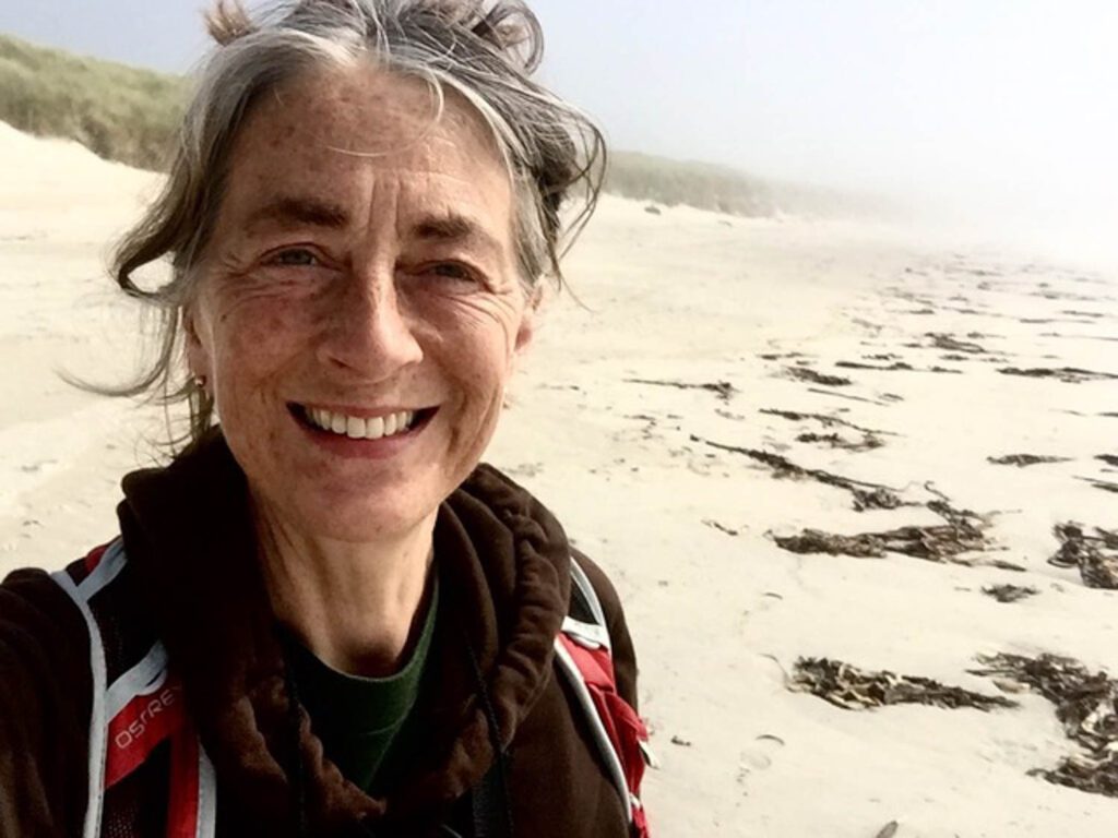 Jane Atfield on a beach smiling at the camera.