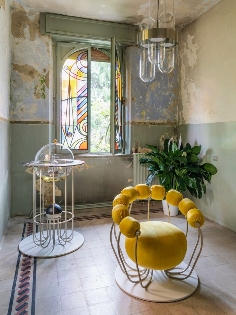 the Insectum furnishing collection, including two 3D-printed glass stained windows, a rug, a mini bar (containing floating insects), an armchair (with 10 arms), and a pendant lamp. 