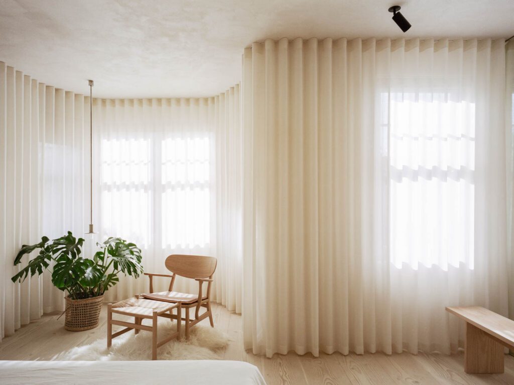 Drapes by The Hackney Draper define the primary bedroom, with a Viabizzuno pendant and Carl Hansen pendant. 