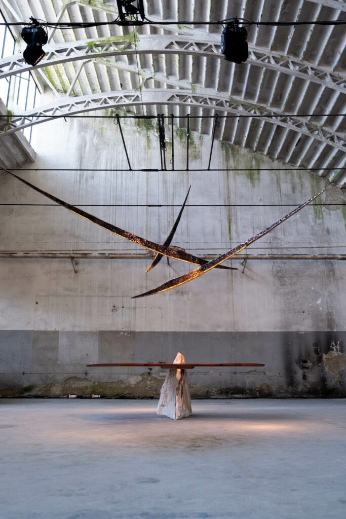 A large raw stone interrupts the hand-shaped wood and stone Fish table by Mircea Anghel. Dangling above, in perfect juxtaposition, is the cast bronze Labia, an LED pendant light by DIM Atelier.