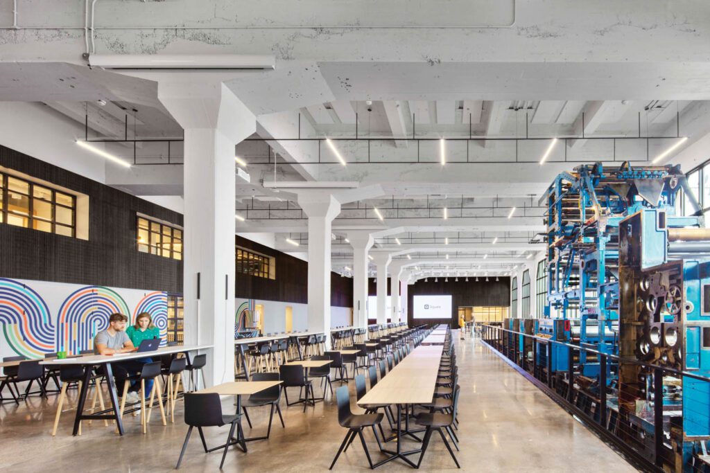 Flanked by the printing press and a Carlos Zamora mural, the vast all-hands area on the ground floor hosts company-wide meetings and serves as a café.