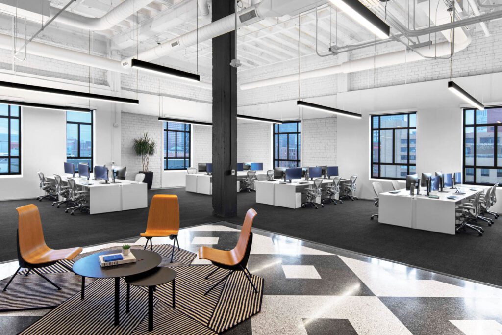 A typical break-out area near benched workstations includes Scolta chairs, Jørgen Møller coffee tables, and a tufted wool rug on a patch of original terrazzo flooring.