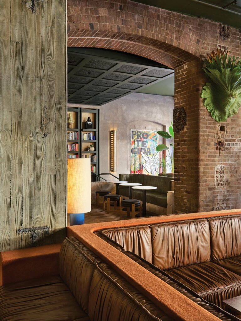 Original brickwork and board-formed concrete frame a view of the lobby library featuring an artwork by Nadia Hernández and shelves backed with rattan wallcovering.