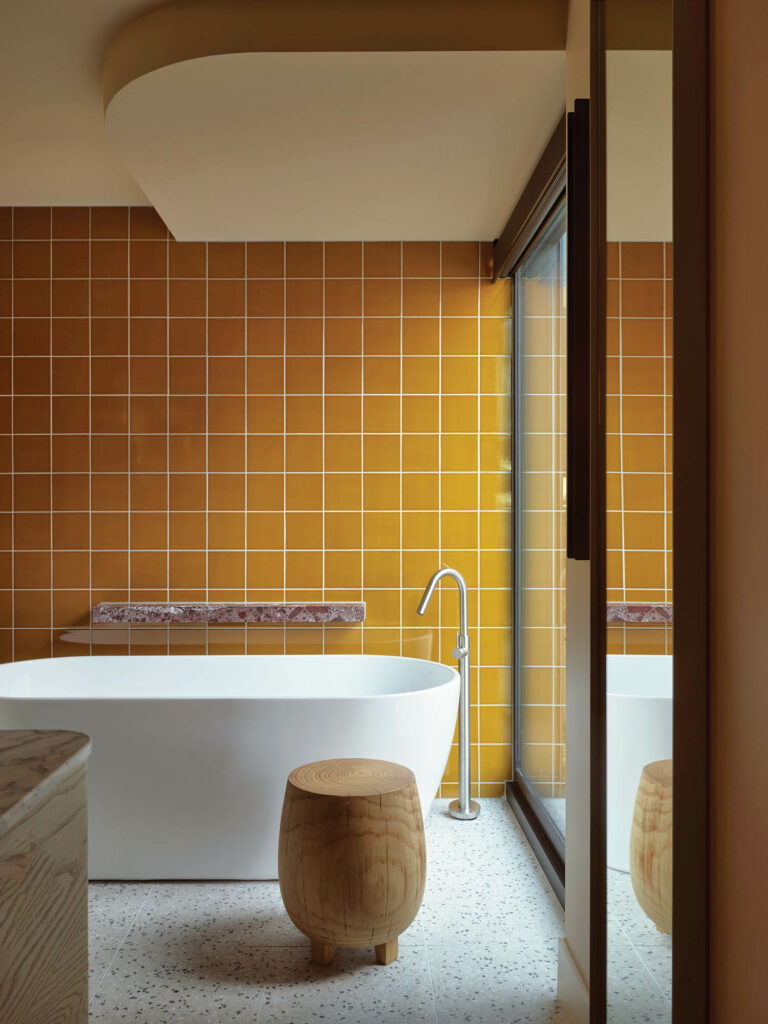 A custom solid-oak stool joins the freestanding tub in a terrazzo-floored guest bathroom.