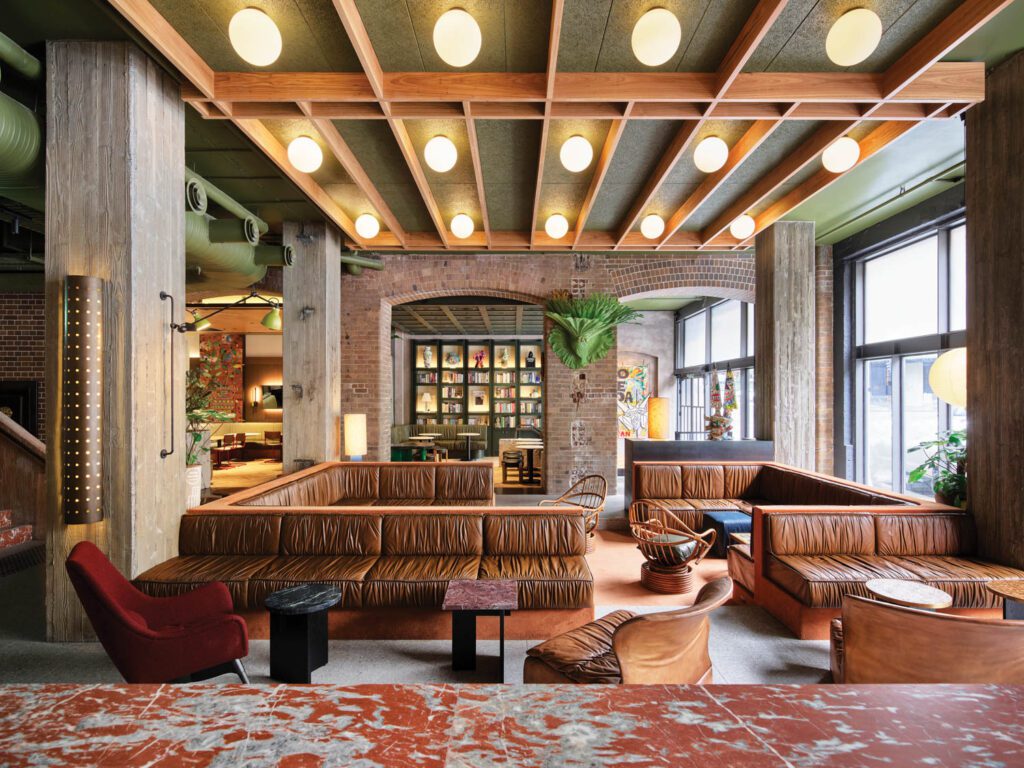 Vintage rattan armchairs join custom banquettes upholstered with ruched leather in the sunken lobby lounge where flooring is custom terrazzo tile and brickwork is original to the 1916 building.