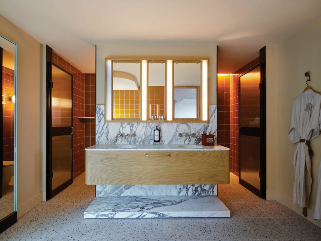 Honed Arabescato Corchia marble forms a plinth and backdrop for a suite bath­room’s custom vanity and mirror.