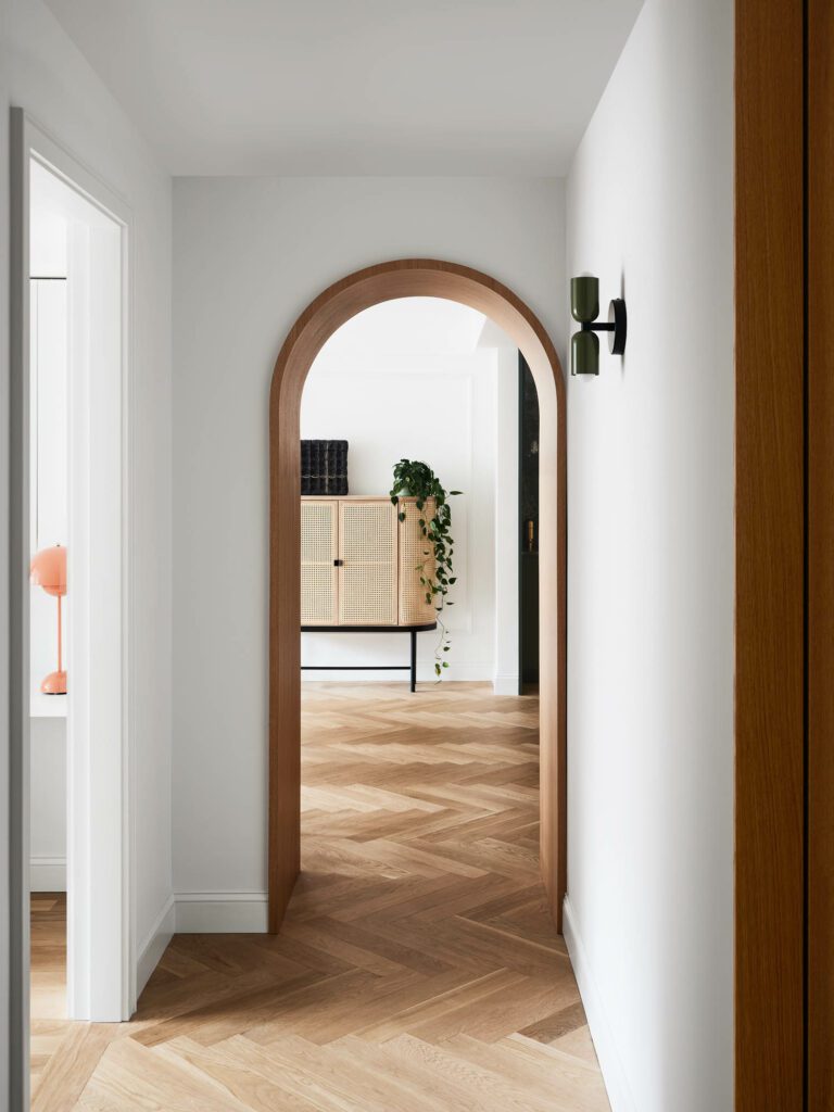 A herringbone hallway frames a view of the living room’s cane sideboard by Warm Nordic.