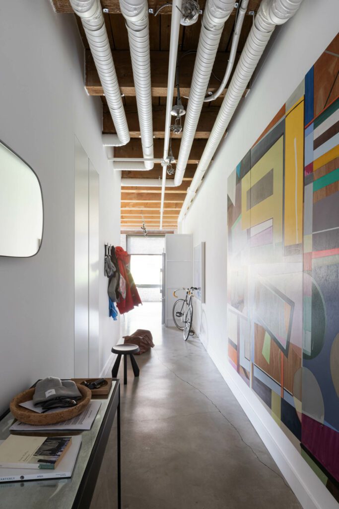 The hallway features exposed pipes, signaling the building's industrial roots. 