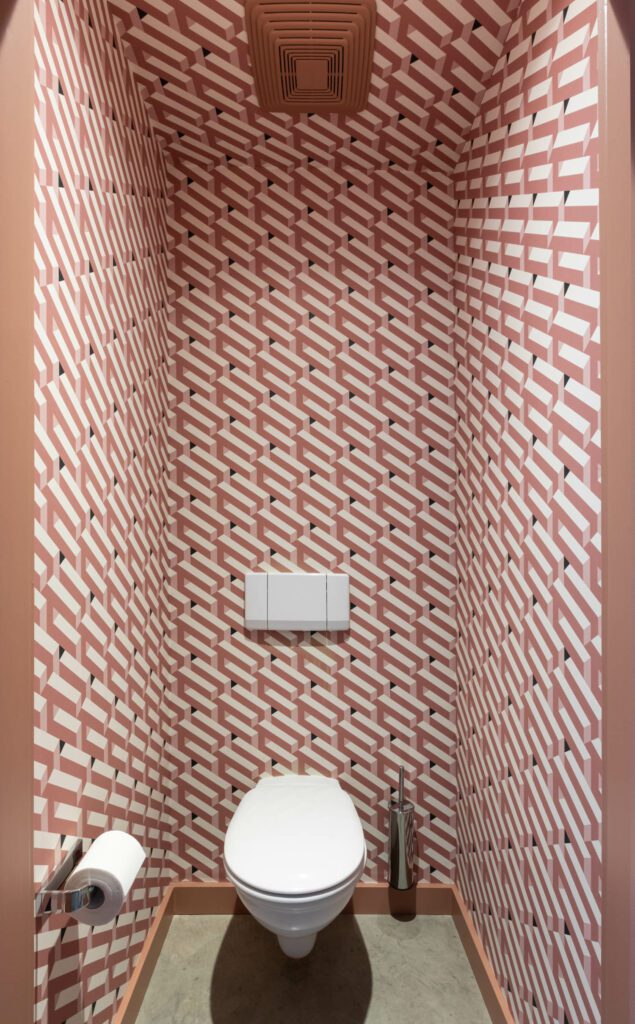 More geometric wallcoverings encircle the toilet, like this one is peach with repeating white lines. 