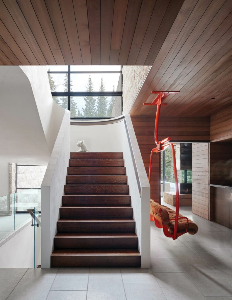 A repurposed chairlift hangs at the foot of the oak staircase, which has a plaster surround.