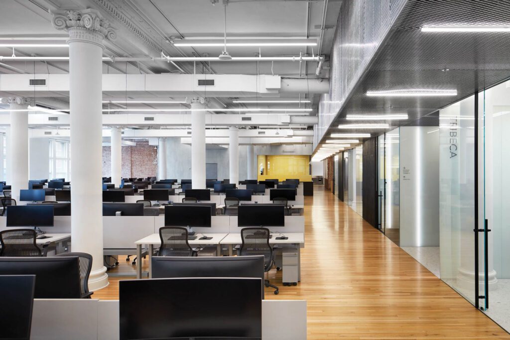 Surface-mounted LED tubes on a metal-mesh soffit demarcate a perimeter circulation corridor in the office area. 