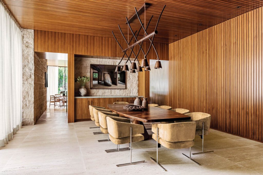 Jorge Zalszupin armchairs set the tone in the dining room, with walls and ceiling clad in Burmese teak; the Haywire chandelier is by David Krynauw. 