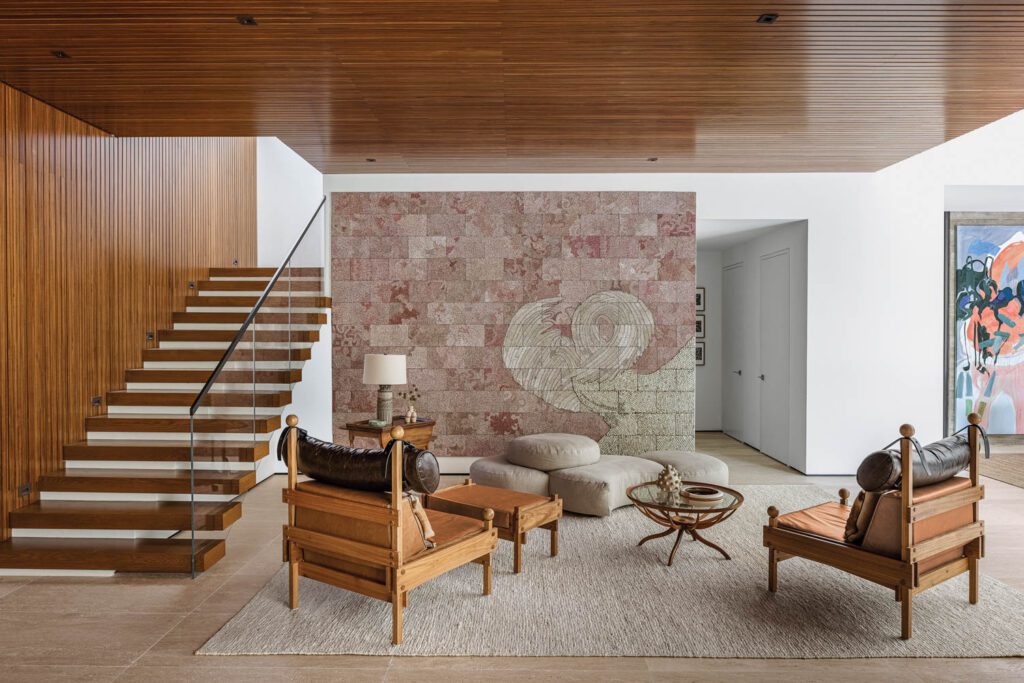 The conversation area between the living and dining rooms feature a Giuseppe Scapinelli coffee table, Sergio Rodrigues armchairs, and Elias Sime’s Tightrope: I Want to Slow Down and Think, 2017.