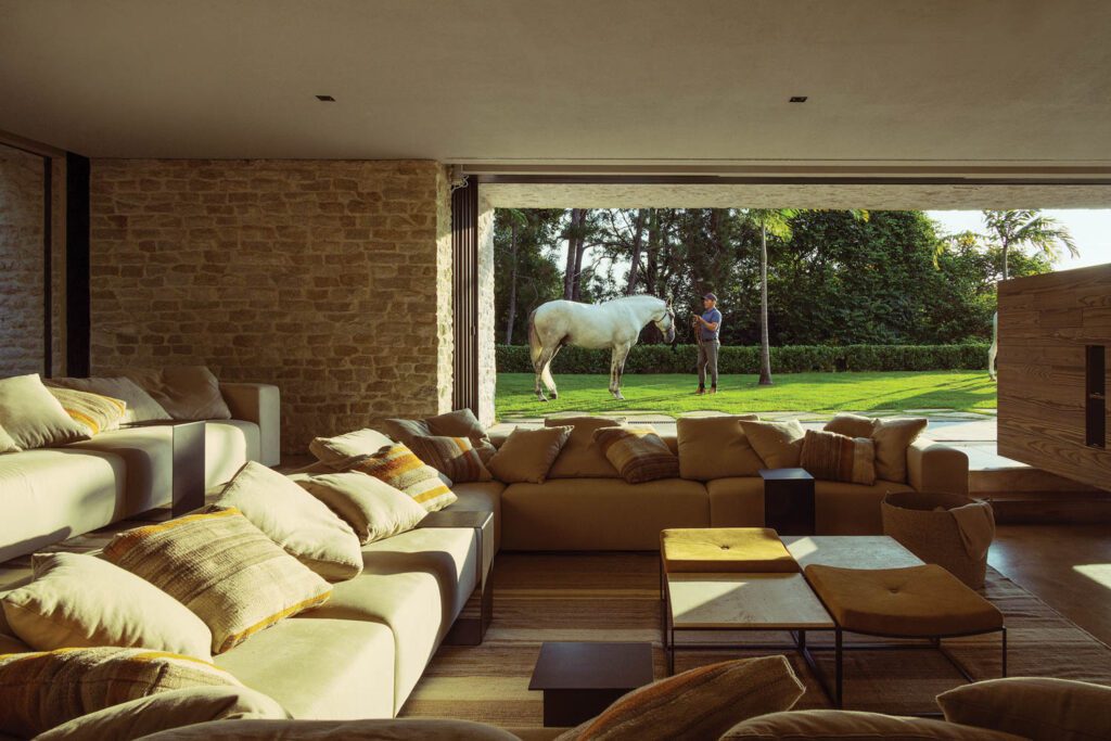 The conversation pit–style home theater is outfitted with pillow-strewn linen-upholstered sofas, a quartet of Jorge Zalszupin’s Capri side tables topped in travertine and suede cushions, and an Indian wool-and-cotton kilim rug.