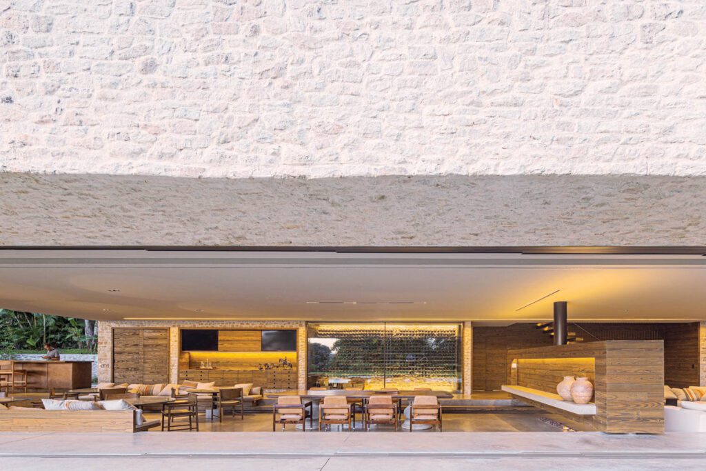 Backed by a bar and glass-enclosed wine cellar, the sunken dining area includes built-in banquettes, round tables of Casa’s design surrounded by Bernardo Figueiredo’s cane-seat chairs, and a large family-heirloom table for 10 flanked with Rodrigues’s leather-upholstered Kiko chairs on casters; the stairs on the right lead to the spa, massage room, and gym. 