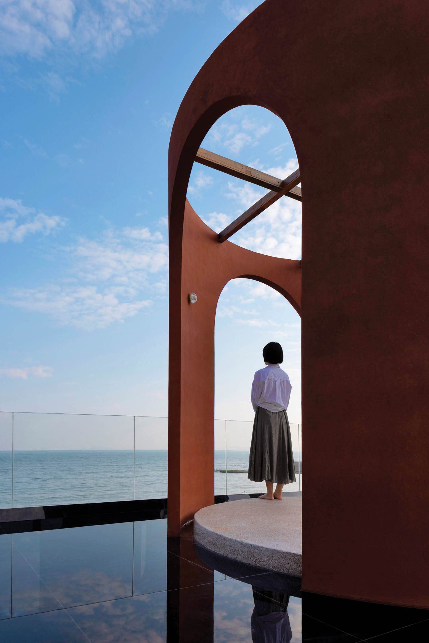 a woman stands next to an open arch looking out over the sea