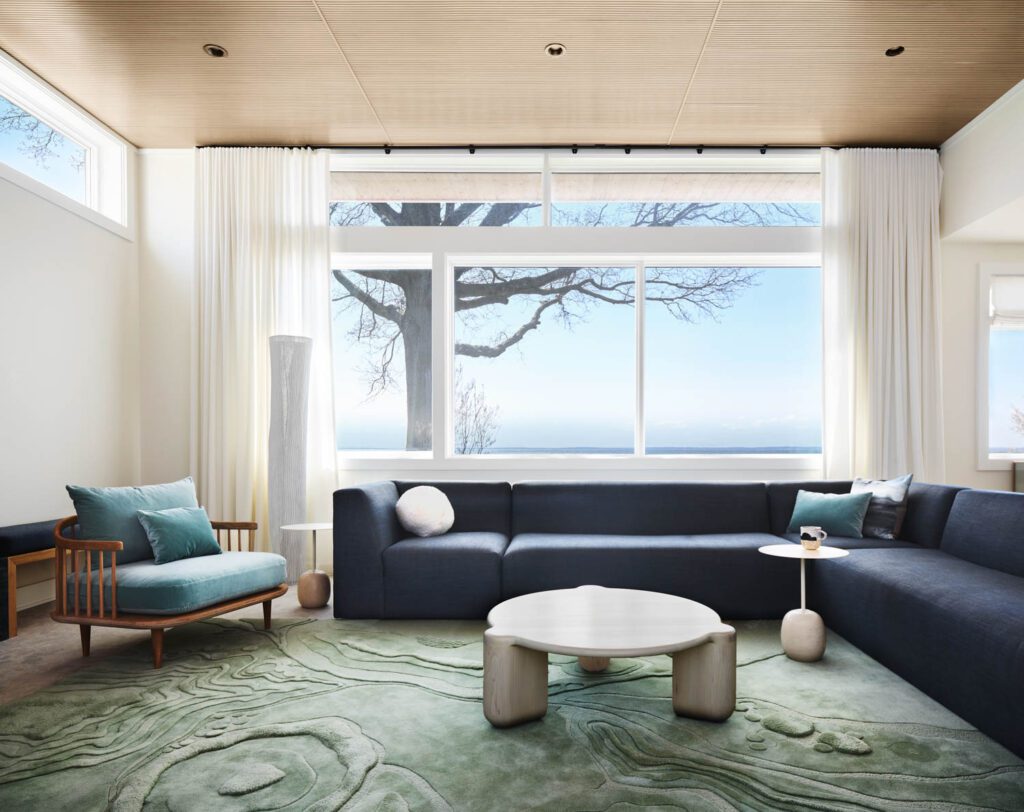 a living room furnished with a long black sectional, armchair and green rug