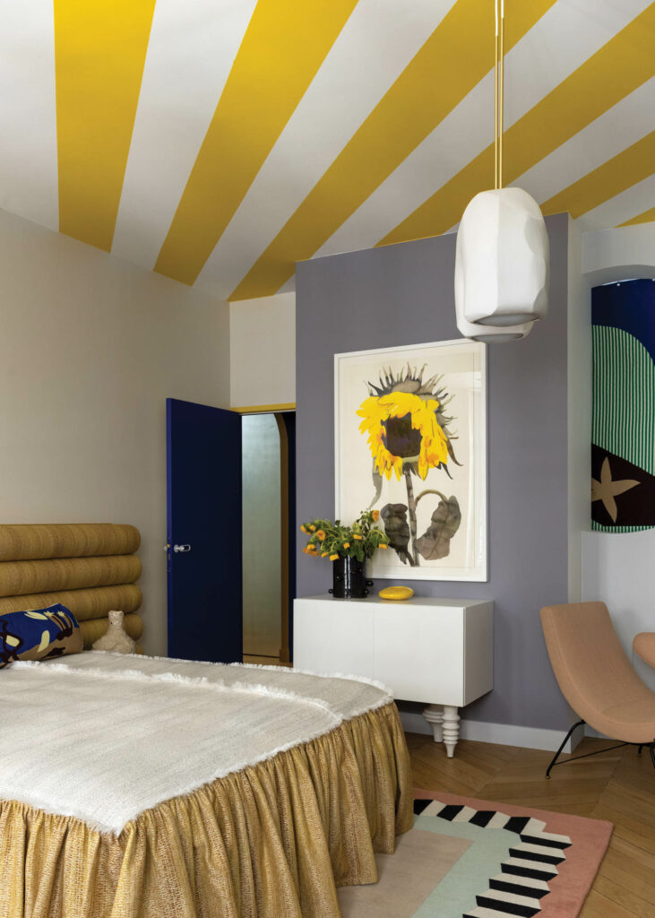 the sunny bedroom of a French apartment with yellow striped ceiling