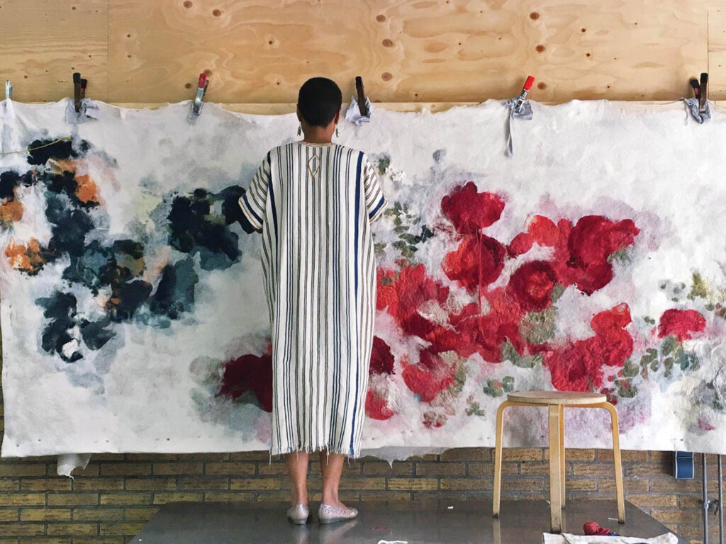 a woman embroidering a wool, silk, and mohair wall hanging