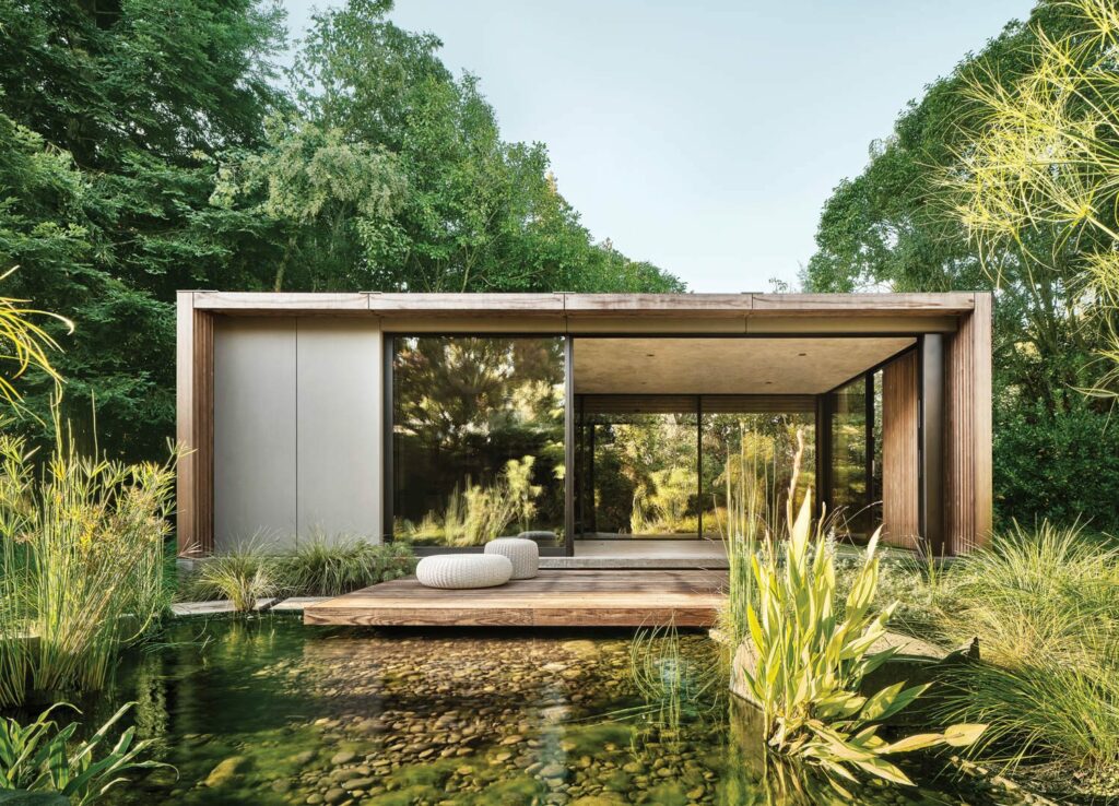 a glass home surrounded by a lush pond