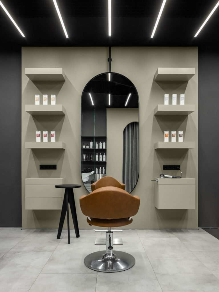 The hair salon design includes a reddish orange armchair in front of a curved mirror. 