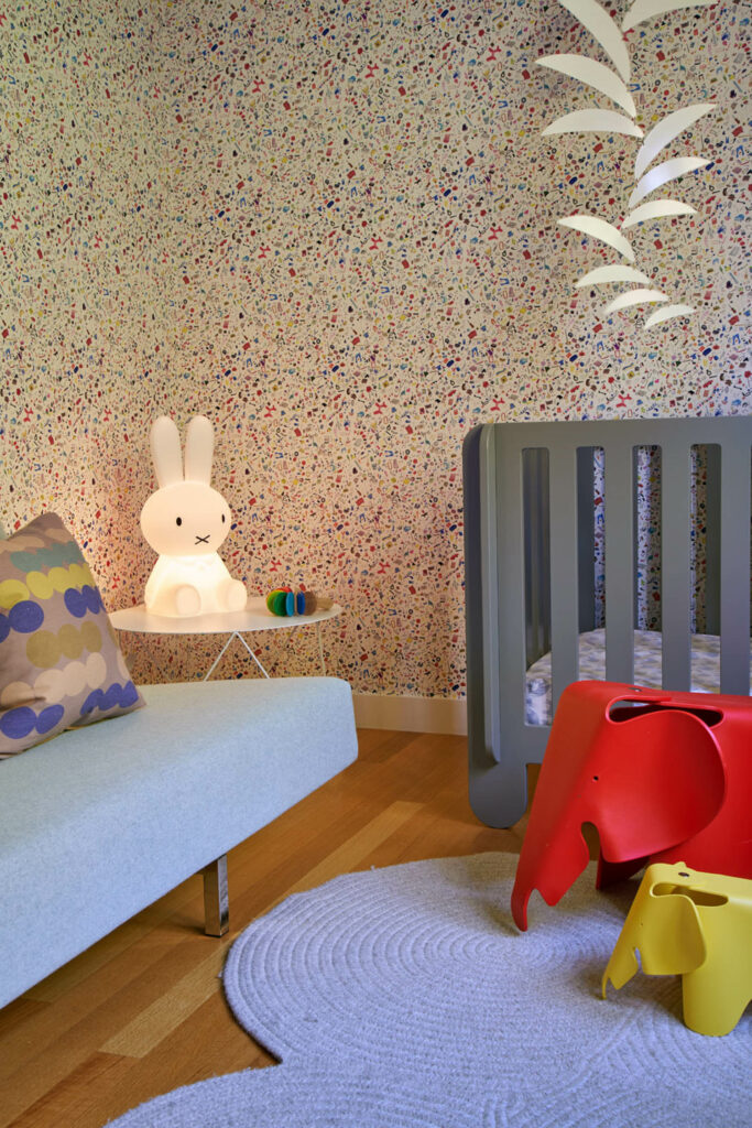 A nursery with floral wallpaper and a bunny lamp with a gray crib.